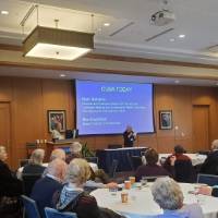 A woman holds a microphone while people at tables listen